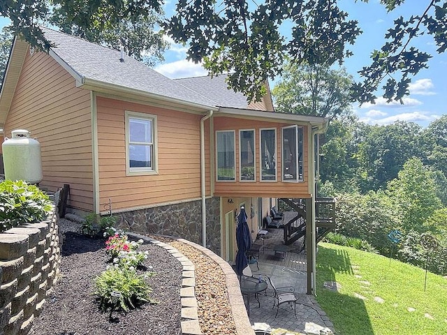 rear view of property with roof with shingles, a patio, a lawn, a sunroom, and stone siding