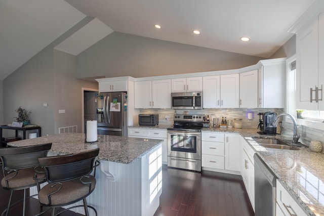 kitchen featuring lofted ceiling, sink, light stone counters, stainless steel appliances, and white cabinets