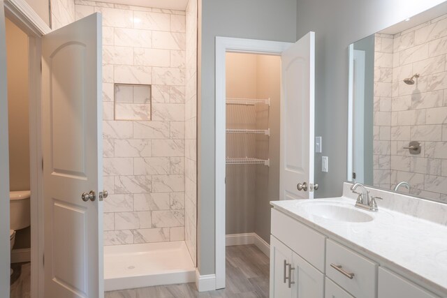 bathroom with hardwood / wood-style flooring, vanity, toilet, and a tile shower