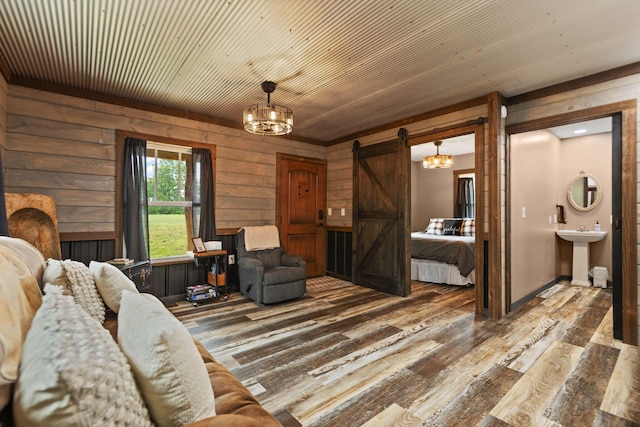 living room with an inviting chandelier, wooden walls, a barn door, hardwood / wood-style flooring, and sink