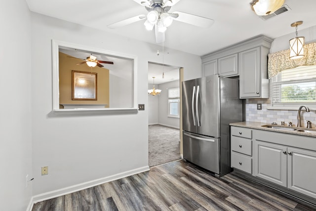 kitchen with backsplash, sink, ceiling fan with notable chandelier, dark carpet, and stainless steel refrigerator