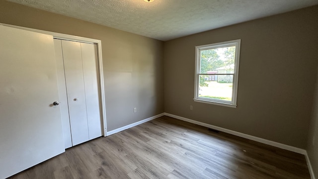 unfurnished bedroom featuring a closet, a textured ceiling, and light wood-type flooring