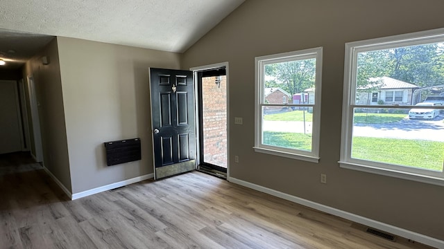 entryway featuring heating unit, lofted ceiling, light hardwood / wood-style floors, and a textured ceiling