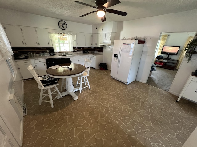 kitchen with a textured ceiling, white cabinets, ceiling fan, sink, and white fridge with ice dispenser