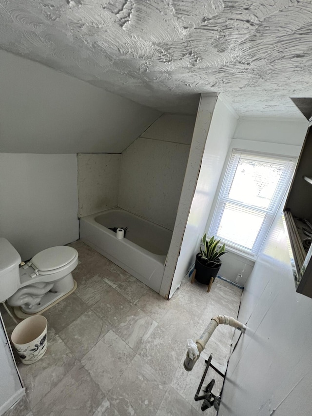 bathroom featuring a textured ceiling, toilet, a bathing tub, and lofted ceiling