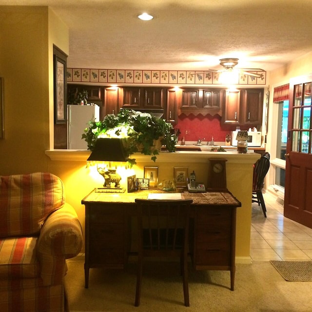 kitchen with a textured ceiling, a breakfast bar area, kitchen peninsula, white refrigerator, and light tile patterned flooring