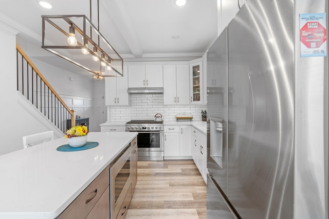 kitchen with under cabinet range hood, stainless steel appliances, light countertops, ornamental molding, and light wood finished floors