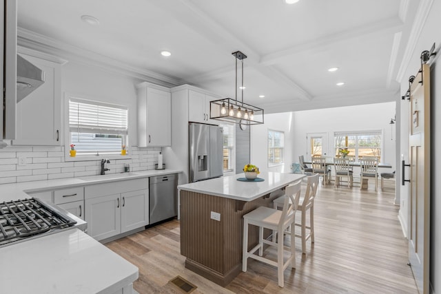 kitchen with a barn door, stainless steel appliances, a kitchen island, a sink, and visible vents