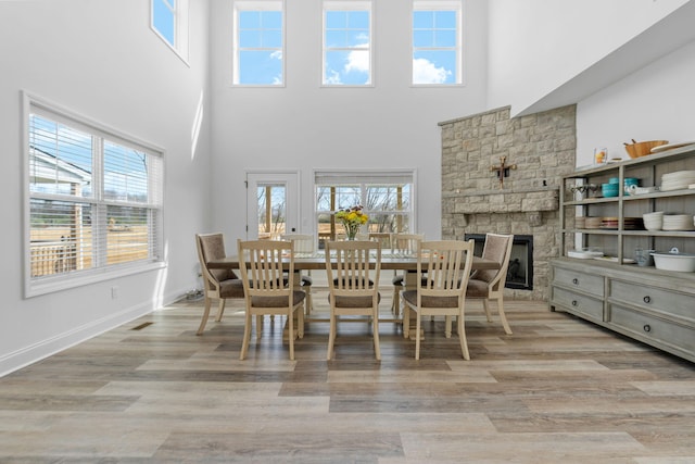 dining space featuring visible vents, a stone fireplace, baseboards, and wood finished floors