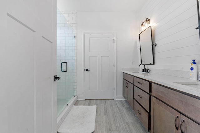 full bathroom with double vanity, a stall shower, a sink, and wood finished floors