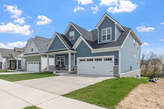 craftsman-style home featuring a shingled roof, concrete driveway, an attached garage, and a front lawn