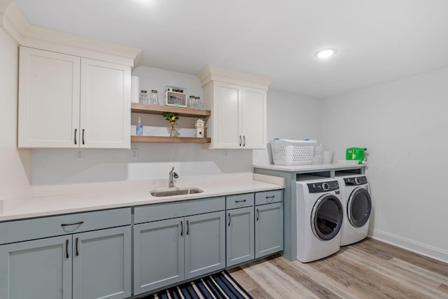 washroom with cabinet space, baseboards, light wood-style floors, washing machine and dryer, and a sink