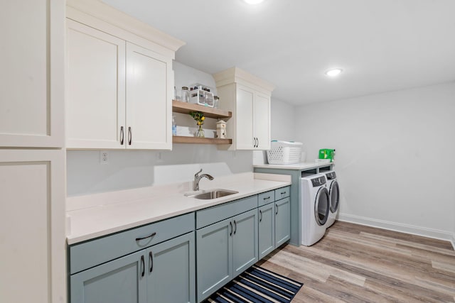 washroom featuring cabinet space, baseboards, light wood-style flooring, washing machine and clothes dryer, and a sink