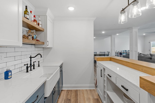 kitchen with open shelves, light wood-style flooring, decorative backsplash, white cabinetry, and ornate columns