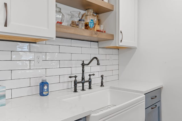 kitchen featuring backsplash, white cabinetry, open shelves, and a sink