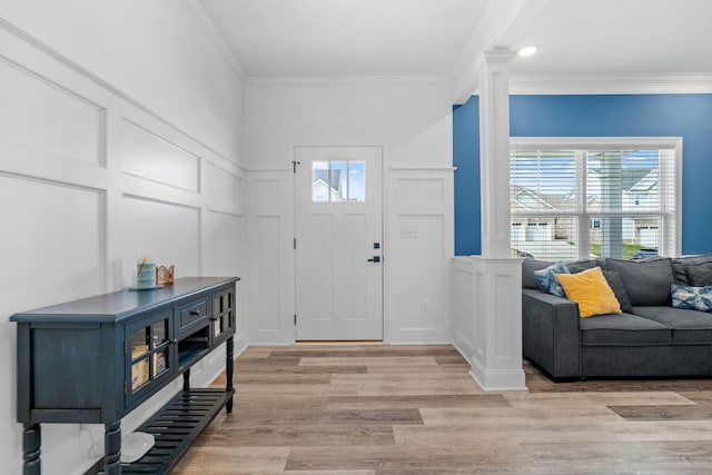 foyer entrance with decorative columns, ornamental molding, a decorative wall, and light wood-style flooring