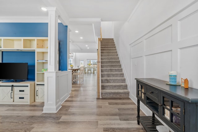 foyer featuring ornamental molding, decorative columns, a decorative wall, and stairs