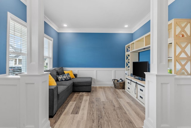 living room featuring light wood-type flooring, a wainscoted wall, crown molding, and ornate columns