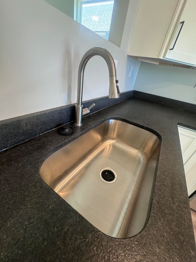 room details featuring sink, white cabinets, and dark stone countertops