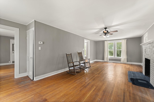 living room with ceiling fan, a brick fireplace, and hardwood / wood-style floors