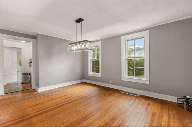 unfurnished dining area featuring a baseboard radiator, crown molding, wood-type flooring, and an inviting chandelier