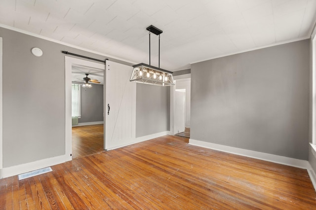 unfurnished dining area with hardwood / wood-style floors, a barn door, ornamental molding, and ceiling fan