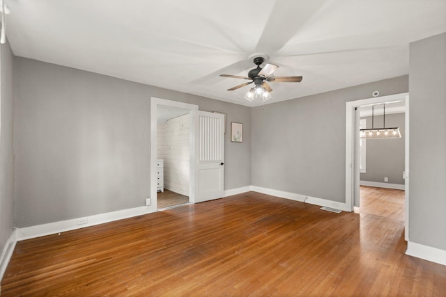 empty room featuring ceiling fan with notable chandelier and hardwood / wood-style flooring