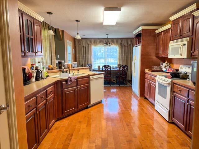 kitchen with white appliances, light hardwood / wood-style flooring, pendant lighting, and sink