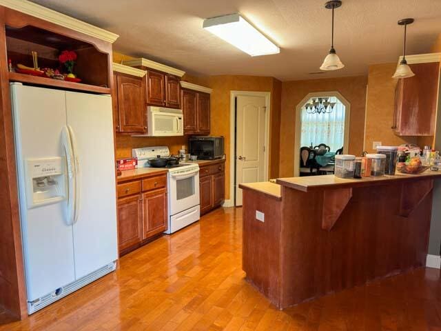 kitchen featuring white appliances, light wood-type flooring, a breakfast bar, pendant lighting, and kitchen peninsula