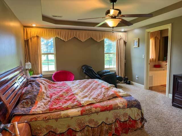 carpeted bedroom with ceiling fan, ensuite bathroom, and a tray ceiling