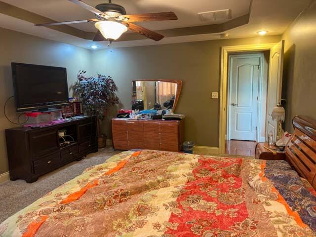 bedroom with ceiling fan, a tray ceiling, and light colored carpet