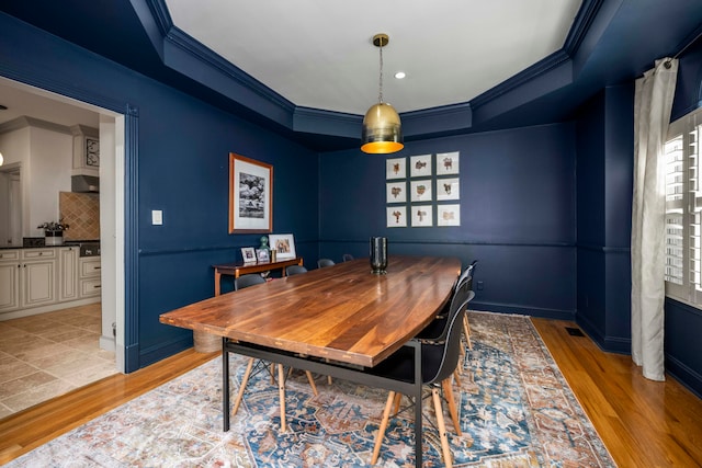 dining area featuring light hardwood / wood-style floors, a raised ceiling, and crown molding