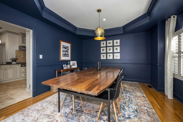 dining room featuring baseboards, light wood-style flooring, ornamental molding, and a tray ceiling