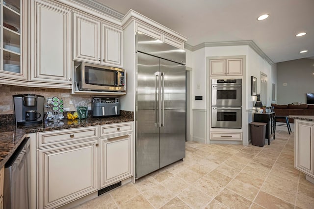 kitchen featuring dark stone counters, crown molding, built in appliances, and tasteful backsplash