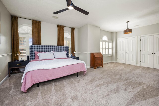 carpeted bedroom with ceiling fan, multiple closets, and multiple windows