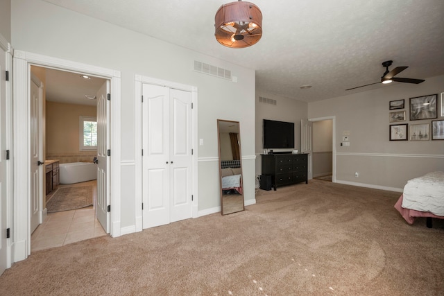 unfurnished bedroom featuring ceiling fan, light carpet, ensuite bathroom, and a textured ceiling