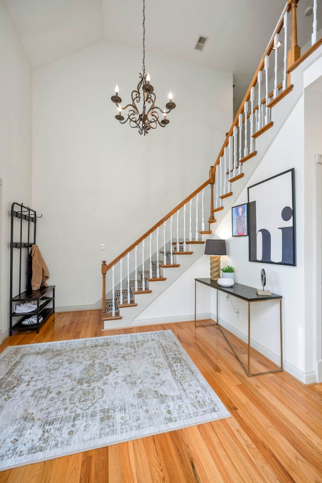 stairway with high vaulted ceiling, hardwood / wood-style floors, and a chandelier