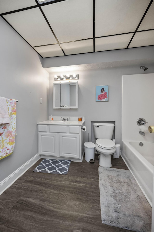 bathroom featuring baseboards, bathing tub / shower combination, toilet, wood finished floors, and vanity