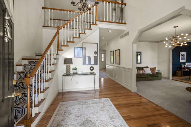 foyer with a notable chandelier, a high ceiling, wood finished floors, visible vents, and stairs