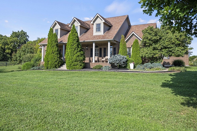 cape cod house with brick siding, a porch, a front yard, and a shingled roof