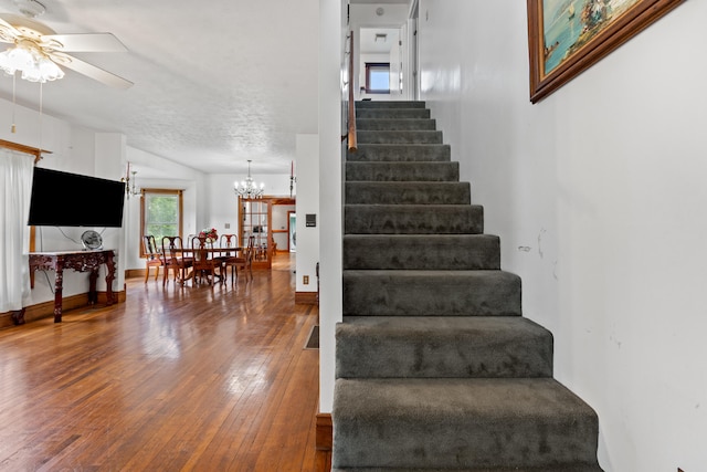 staircase with a textured ceiling, ceiling fan with notable chandelier, and hardwood / wood-style flooring