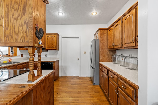 kitchen featuring sink, a textured ceiling, light hardwood / wood-style floors, and stainless steel refrigerator