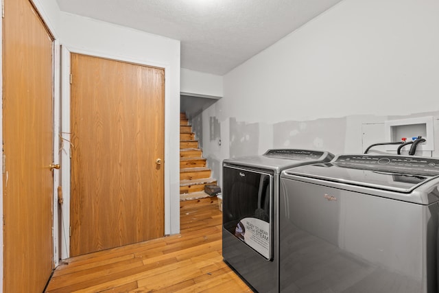 clothes washing area with rustic walls, separate washer and dryer, a textured ceiling, and light hardwood / wood-style floors