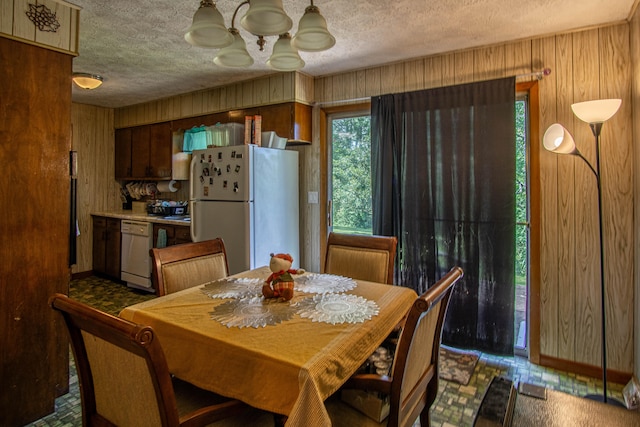 dining room with wood walls, a textured ceiling, and an inviting chandelier