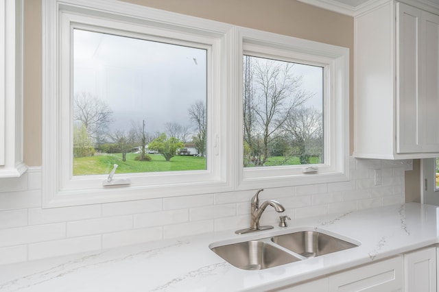 kitchen featuring light stone counters, sink, a healthy amount of sunlight, and white cabinetry