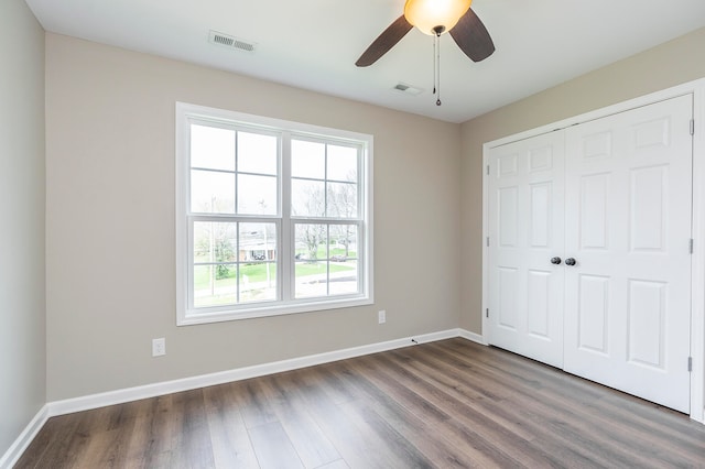 unfurnished bedroom with ceiling fan, a closet, hardwood / wood-style flooring, and multiple windows