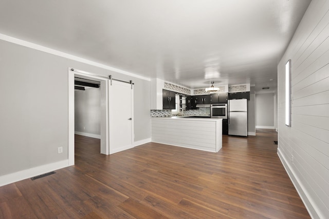 kitchen with decorative backsplash, dark wood-type flooring, a barn door, appliances with stainless steel finishes, and kitchen peninsula