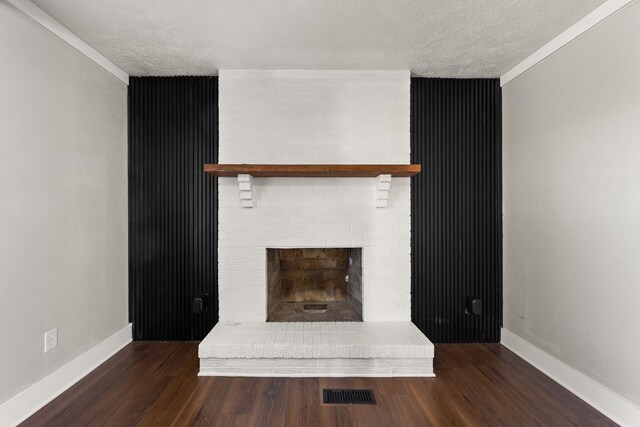 unfurnished living room featuring hardwood / wood-style flooring, brick wall, a textured ceiling, and a brick fireplace