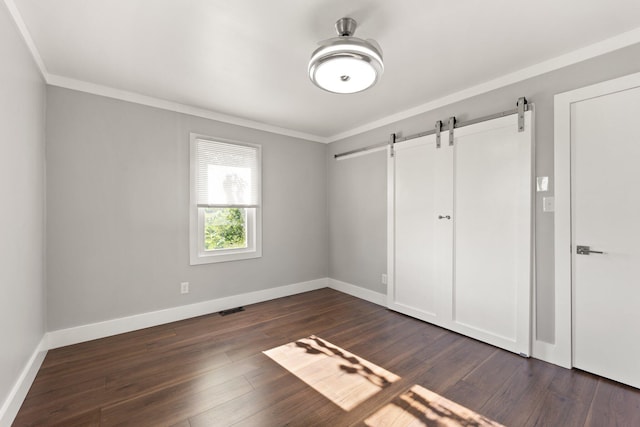 unfurnished bedroom with crown molding, dark hardwood / wood-style floors, and a barn door