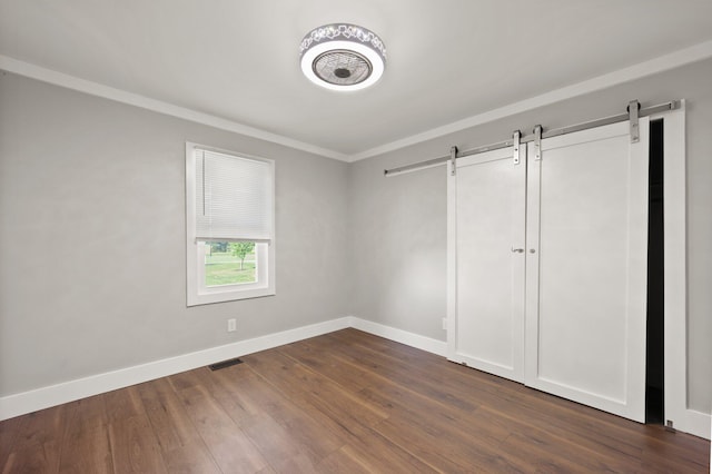 unfurnished bedroom featuring a barn door, hardwood / wood-style floors, and ornamental molding